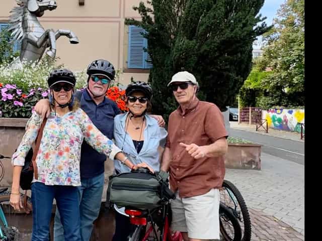 Quatre clients casqués avec leurs vélos de location devant une maison alsacienne