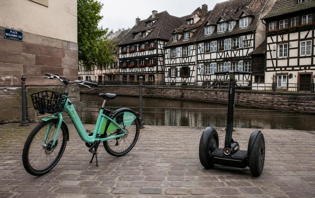 An electric city bike and a self-balancing standing scooter side by side on a Strasbourg canal square